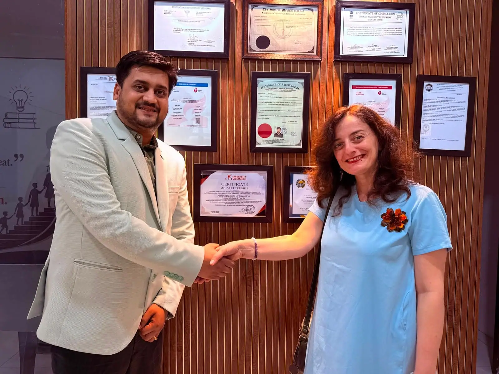 A Doctors Build International representative shaking hands with a colleague in an office hung with certificates