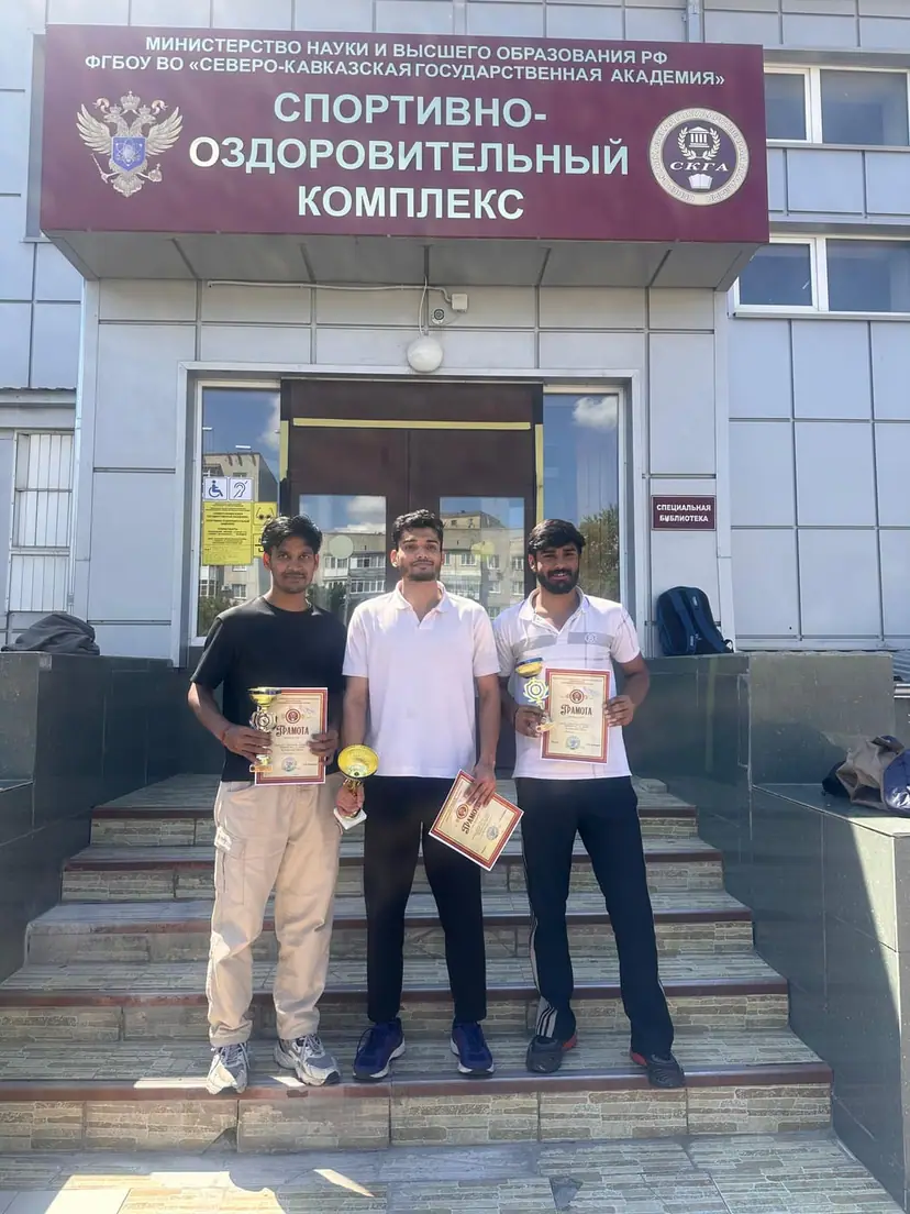Three Indian medical students with trophies and certificates outside the sports and health complex at North Caucasian State Academy
